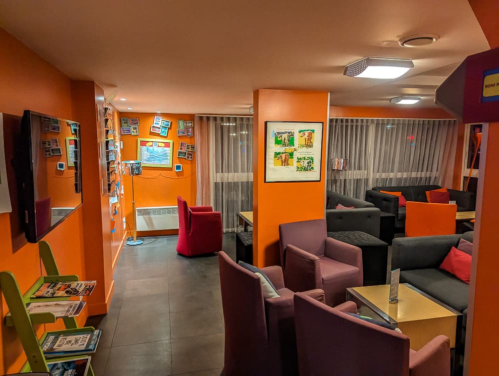 Salon coloré de l'Ibis Styles Ouistreham avec fauteuils violets et orange sous éclairage chaud du soir