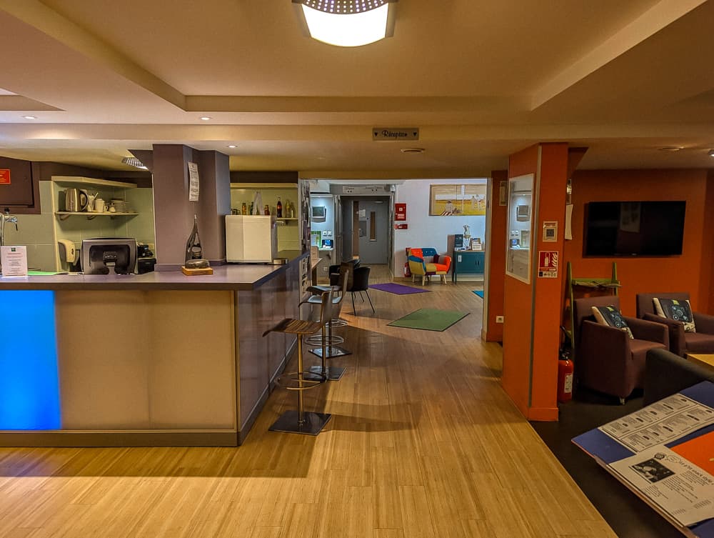 Comptoir d'accueil moderne de l'hôtel Ibis Styles Ouistreham avec coin bar et salle colorée au fond