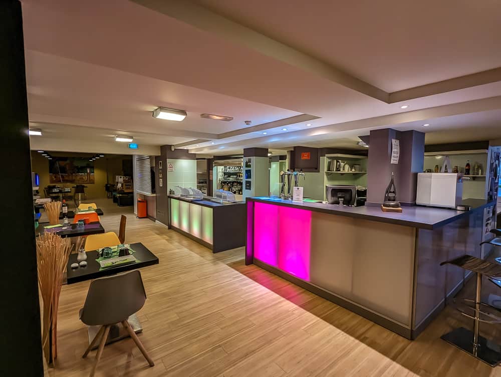Comptoir lumineux moderne du bar de l'Ibis Styles Ouistreham avec tables colorées et ambiance conviviale