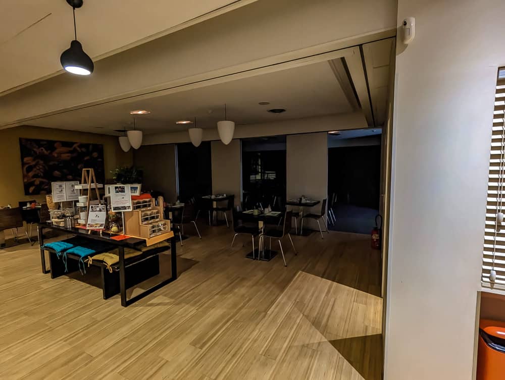 Salle de petit-déjeuner de l'hôtel Ibis Styles Ouistreham avec tables vides et buffet en bois éclairé