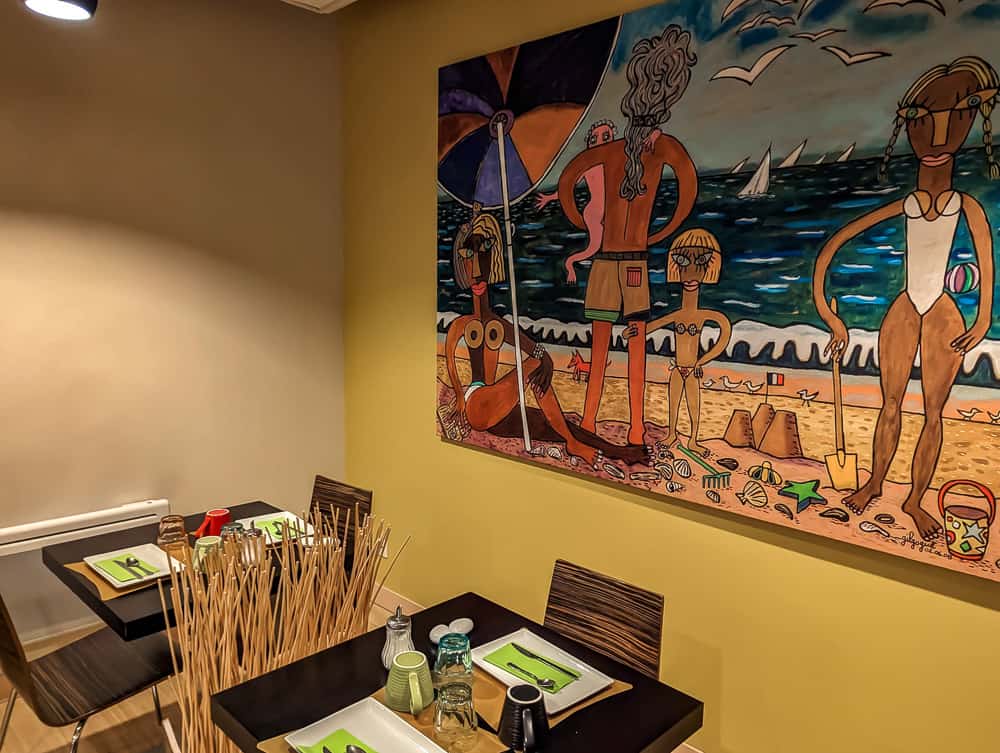 Petite salle de restauration colorée avec tableau représentant une scène de plage et tables dressées
