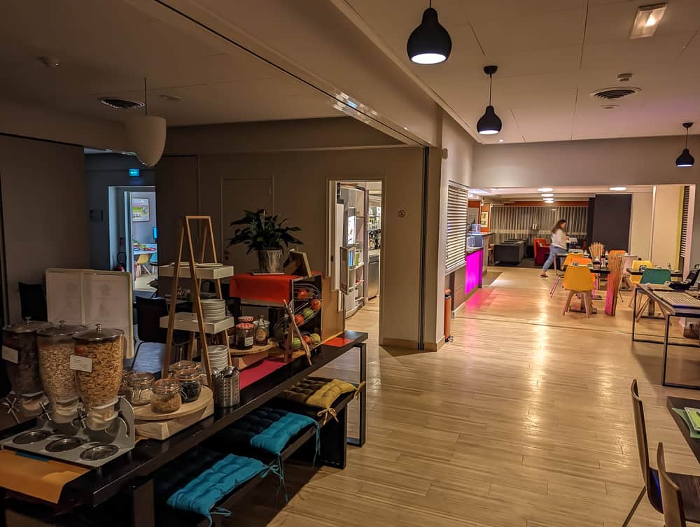 Salle de petit-déjeuner lumineuse de l'hôtel Ibis Styles Ouistreham avec buffet de céréales et tables colorées