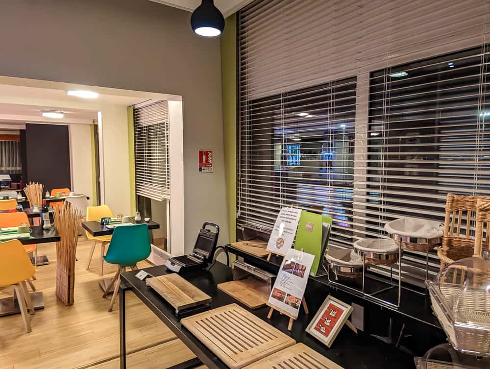 Salle de petit-déjeuner lumineuse avec chaises colorées, tables en bois et buffet à l'hôtel Ibis Styles Ouistreham