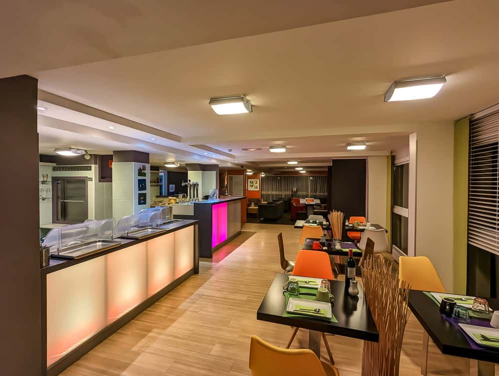 Salle de restaurant moderne à l'Ibis Styles Ouistreham avec chaises colorées et buffet éclairé rose-orangé