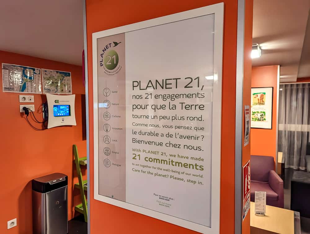 Affiche des engagements écologiques Planet 21 sur un mur orange de l'hôtel Ibis Styles Ouistreham