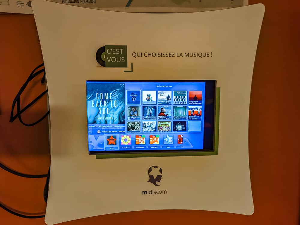 Écran tactile musical Midiscom fixé au mur orange de l'hôtel Ibis Styles Ouistreham