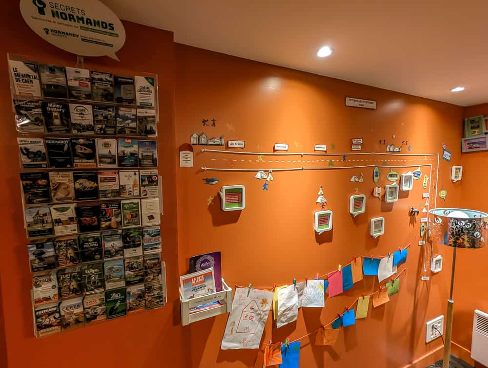 Mur orange décoré de dessins d'enfants, cartes postales et brochures touristiques à l'hôtel Ibis Styles Ouistreham