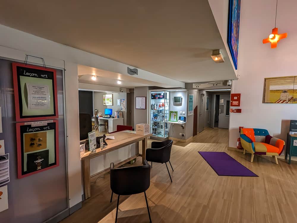 Réception moderne de l'hôtel Ibis Styles Ouistreham avec bureau en bois, fauteuils colorés et présentoir vitré