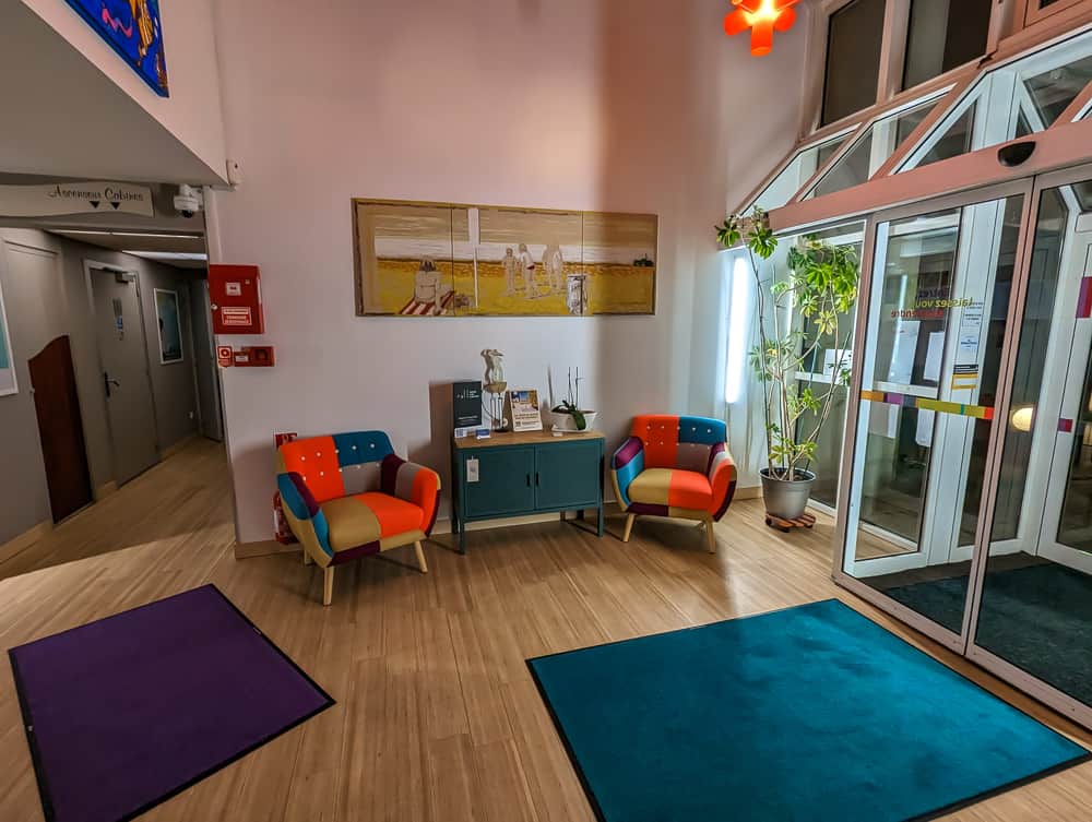 Petit coin d'accueil coloré avec deux fauteuils multicolores, meuble turquoise et plante près de l'entrée vitrée