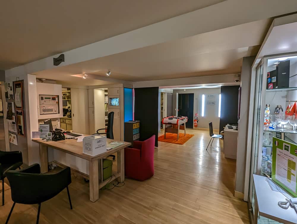 Réception moderne de l'hôtel Ibis Styles Ouistreham avec bureau en bois, baby-foot et présentoir lumineux