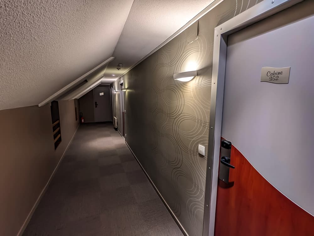 Couloir mansardé de l'hôtel Ibis Styles Ouistreham avec porte de chambre 352 et éclairage mural