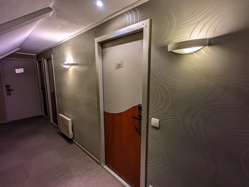 Couloir d'étage de l'hôtel Ibis Styles Ouistreham avec portes de chambres fermées et éclairage mural doux