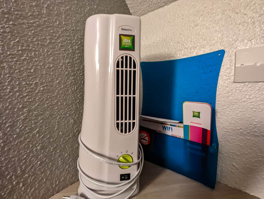 Petit ventilateur blanc Ibis Styles posé sur une table en bois près d'un mur texturé