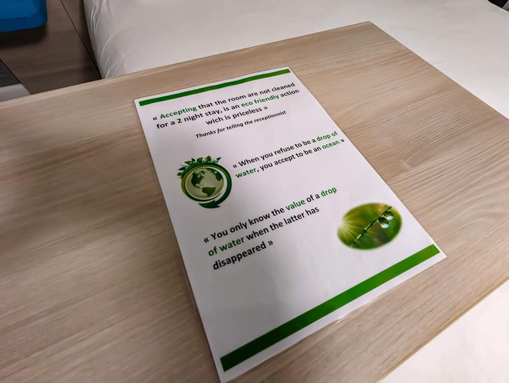 Feuille d'information écologique posée sur une table en bois clair dans une chambre Ibis Styles Ouistreham