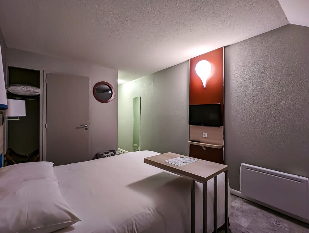 Chambre compacte avec lit double, table en bois, télévision murale et lampe design en forme de ballon