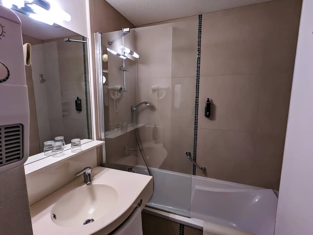 Petite salle de bain moderne avec baignoire-douche, vasque beige, miroir éclairé et mur carrelé beige clair