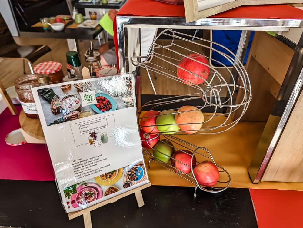 Corbeille métallique avec pommes rouges et vertes sur un buffet de petit-déjeuner à l'Ibis Styles Ouistreham