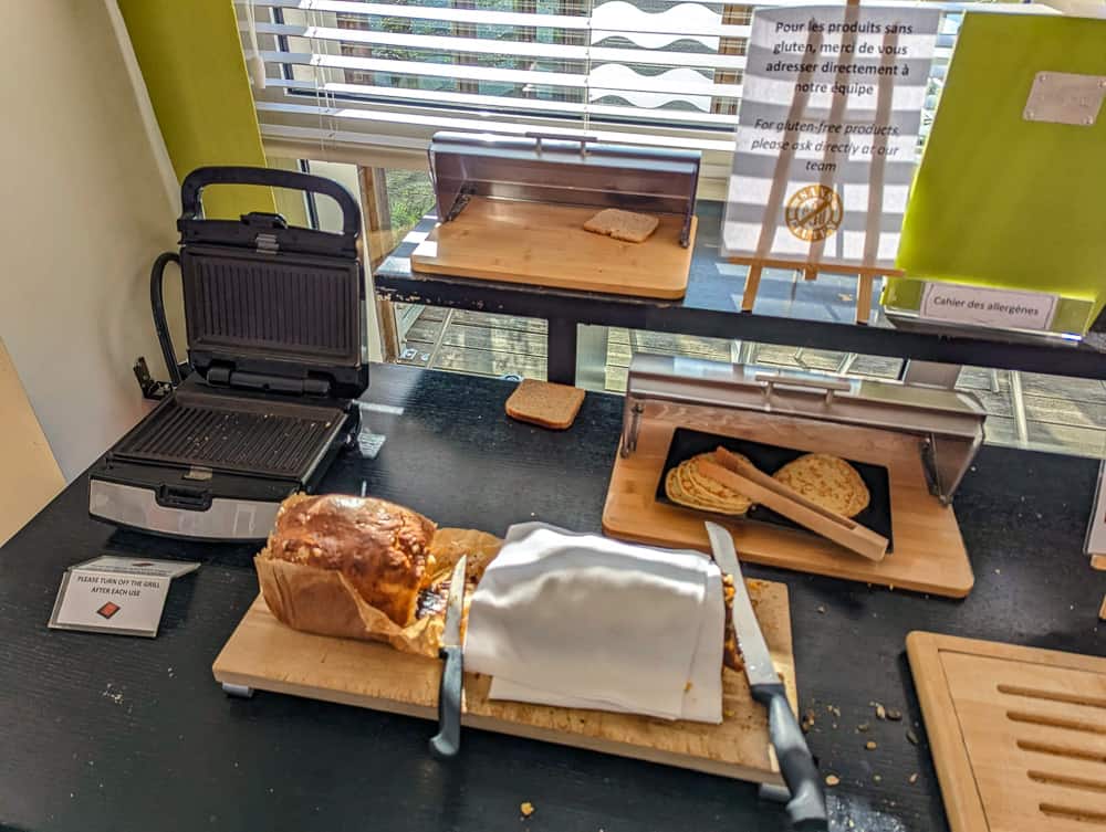 Buffet petit-déjeuner avec gaufrier, tranches de pain, gâteaux et pancartes d'allergènes à l'Ibis Styles Ouistreham