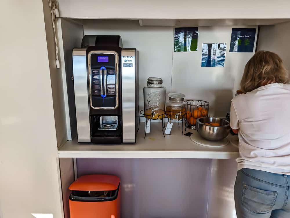 Cliente de dos préparant des oranges près d'une machine à café et distributeurs de jus au buffet Ibis Styles