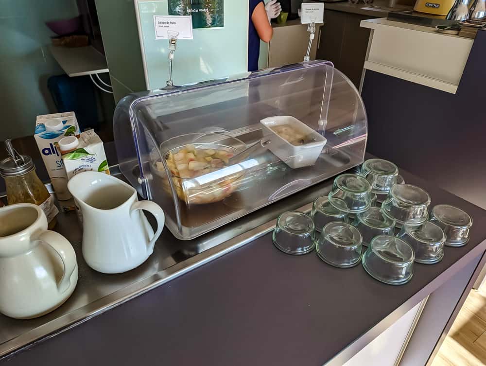 Présentation du buffet petit-déjeuner avec salade de fruits, pichets de lait et verres empilés à l'hôtel