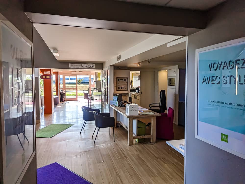 Hall d'accueil lumineux de l'Ibis Styles Ouistreham avec comptoir moderne, chaises colorées et baies vitrées