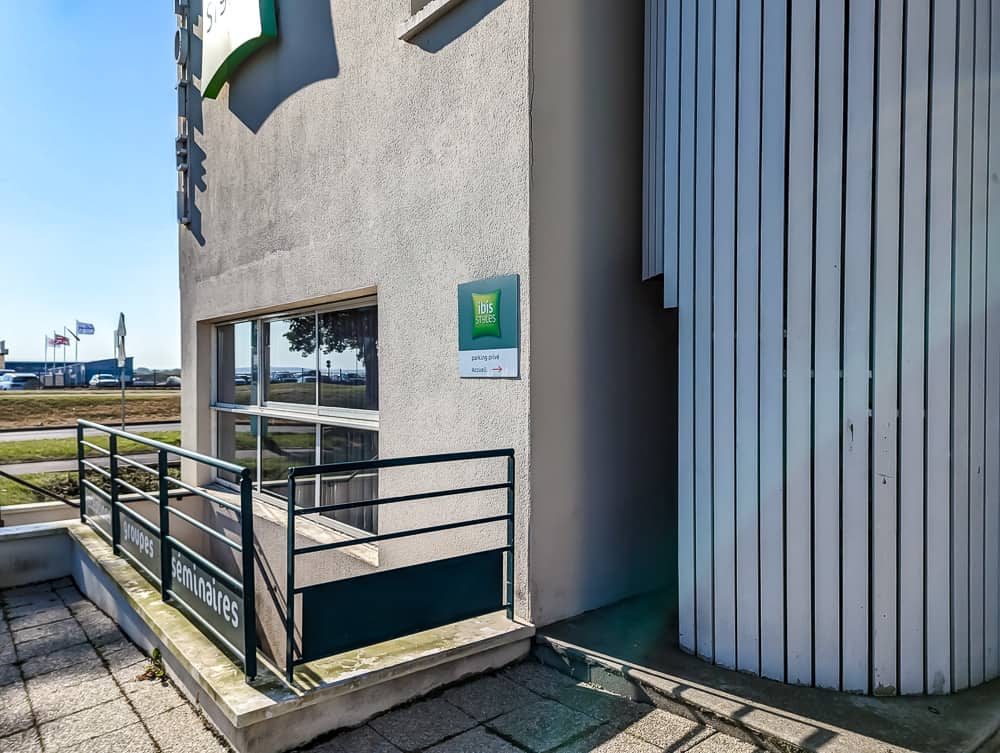 Façade latérale de l'hôtel Ibis Styles Ouistreham avec rampe d'accès et panneau direction parking-garage