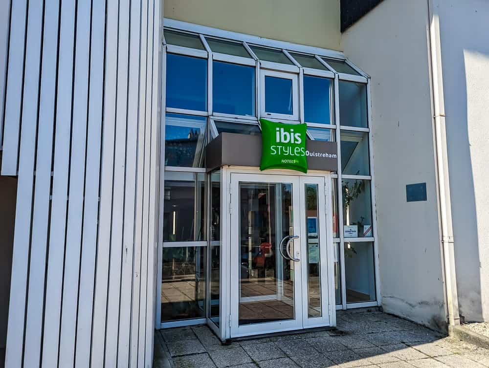 Entrée vitrée de l'hôtel Ibis Styles Ouistreham avec façades claires et enseigne verte bien visible
