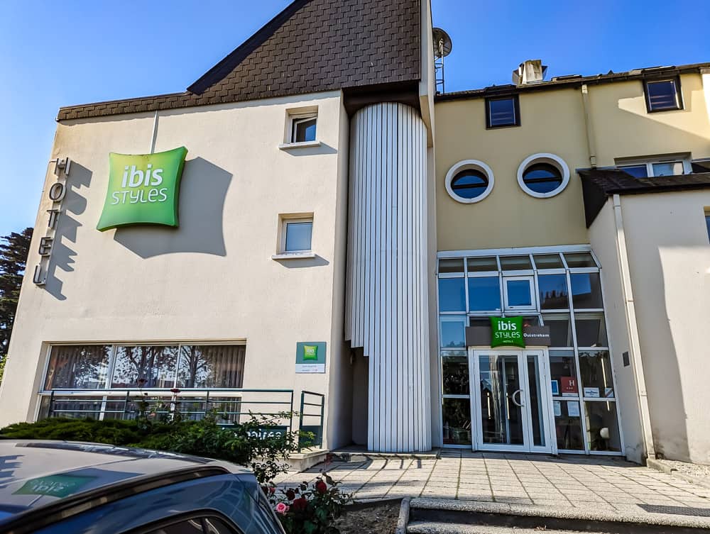 Façade claire de l'hôtel Ibis Styles Ouistreham avec enseigne verte et entrée vitrée sous ciel bleu