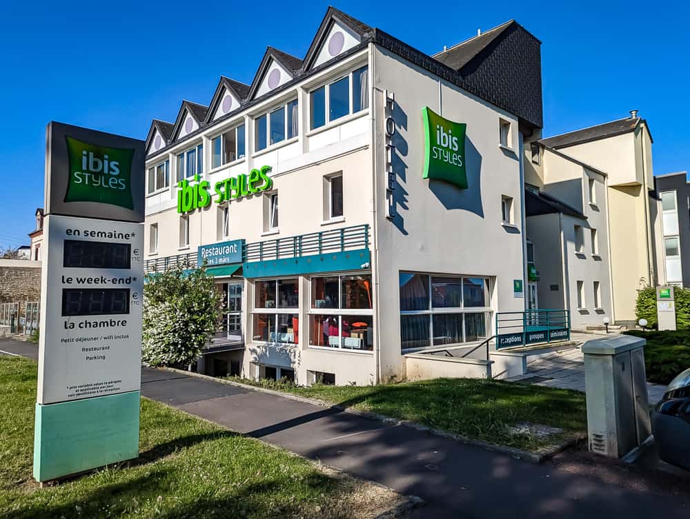 Façade claire de l'hôtel Ibis Styles Ouistreham avec enseigne verte et terrasse vitrée sous ciel bleu