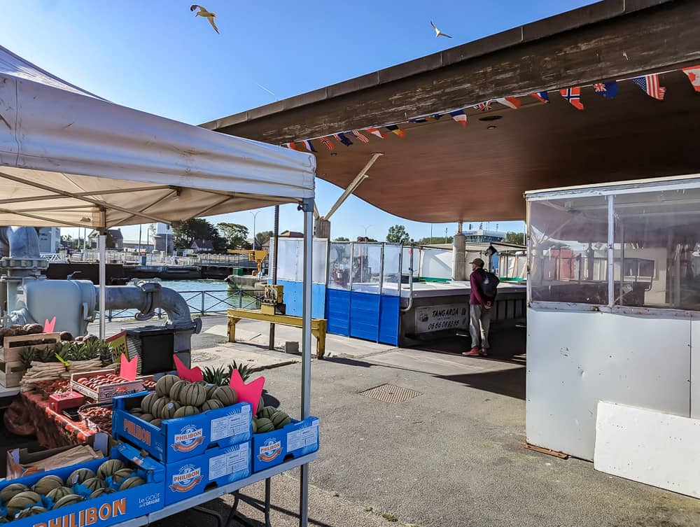 Étals de fruits et légumes sous un auvent au port d'Ouistreham par une journée ensoleillée