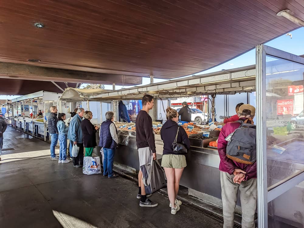 Des clients attendent devant un étal de poisson couvert, sous un toit en bois à Ouistreham