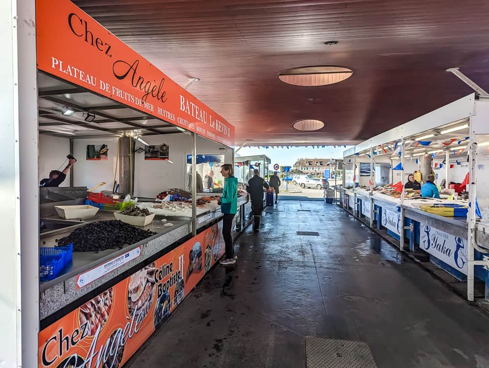 Marché couvert à Ouistreham avec étals de fruits de mer frais et clients discutant avec les vendeurs