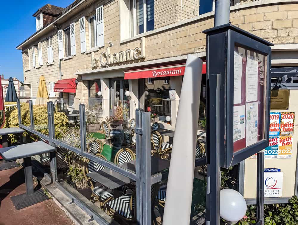 Façade en pierre beige du restaurant avec terrasse extérieure et chaises rayées vert et blanc à Ouistreham