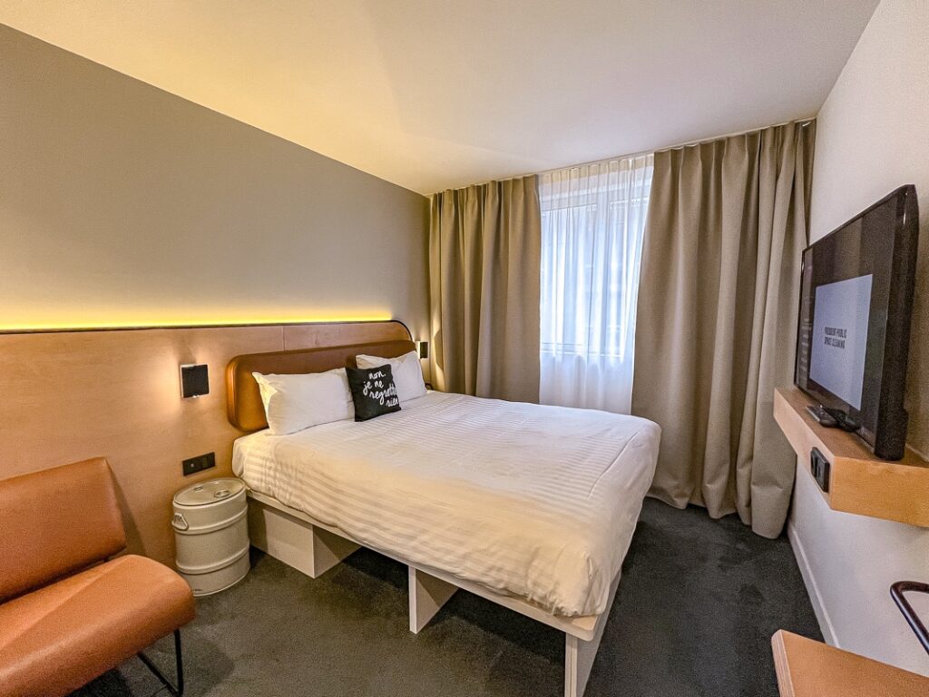 Chambre moderne du Moxy Paris Bastille avec lit double, coussin décoratif noir et lumière d'ambiance.