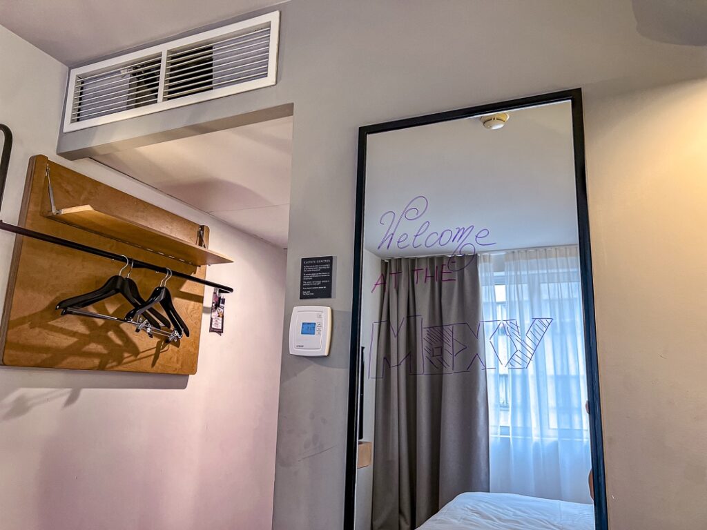 Coin d'une chambre du Moxy Paris Bastille avec miroir Welcome at the Moxy et penderie en bois.