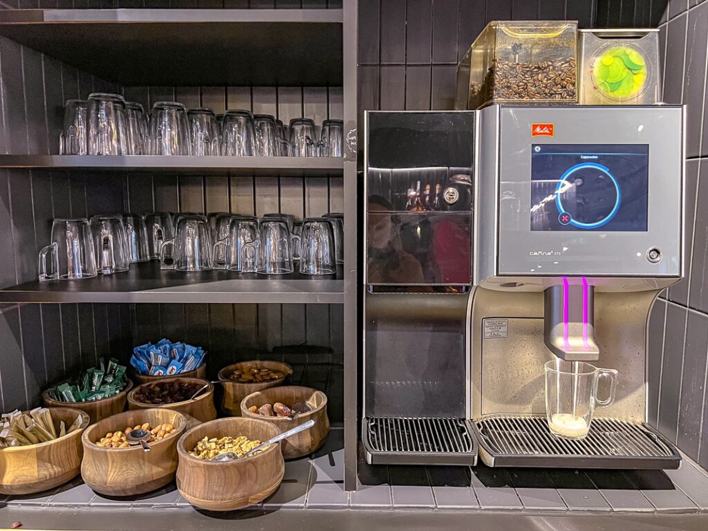 Machine à café automatique avec tasse en verre, bols de collations et étagères remplies de verres propres.