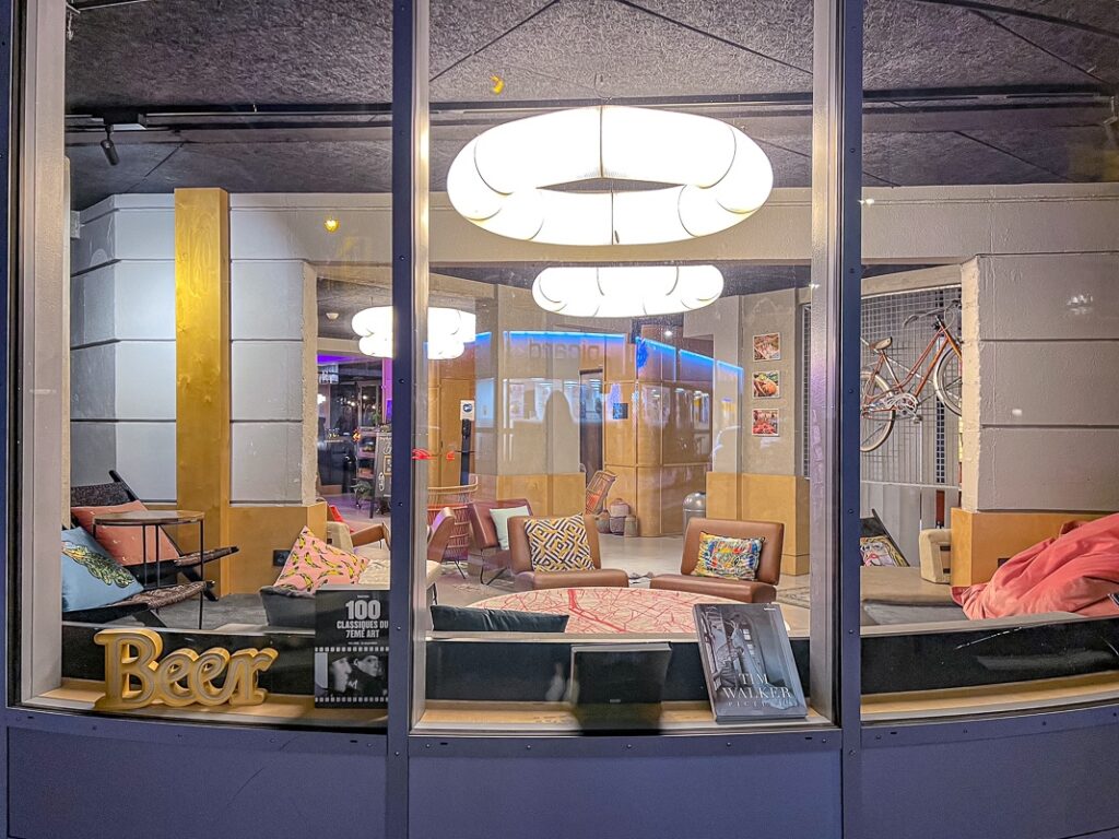 Salon moderne du Moxy Paris Bastille avec fauteuils colorés, coussins décoratifs et vélo mural visible.