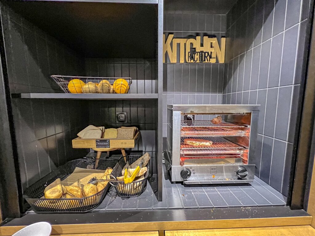 Étagère de buffet avec pains variés, oranges en panier métallique et grille-pain en inox allumé.