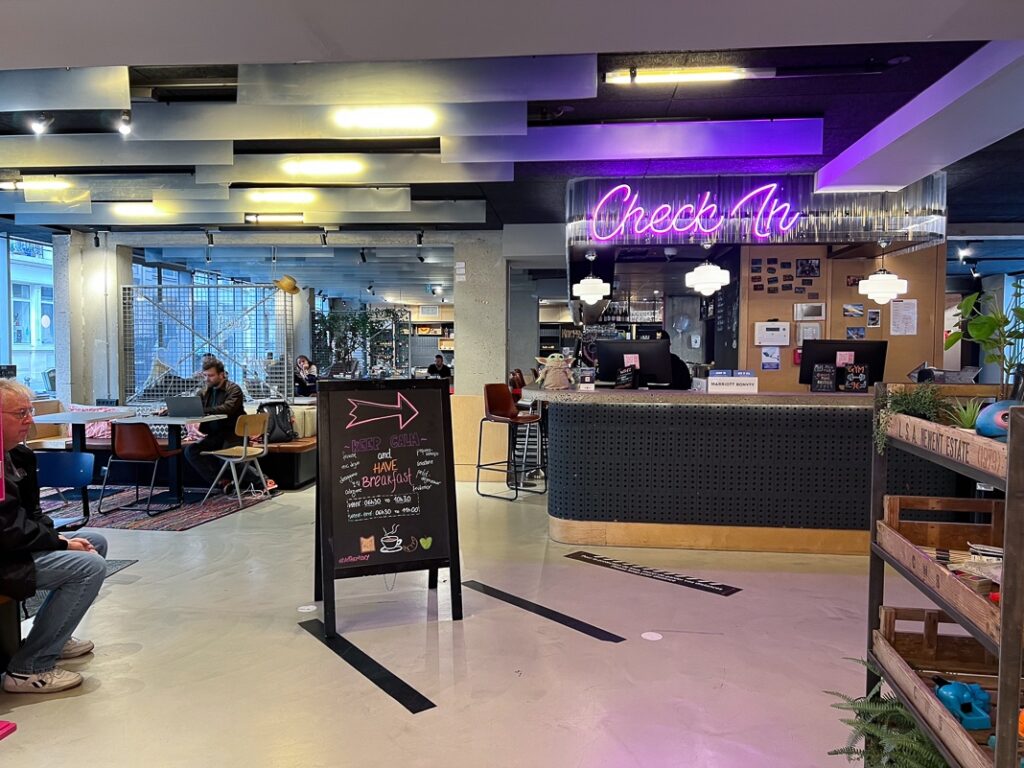 Hall d'accueil moderne du Moxy Paris Bastille avec comptoir check-in éclairé au néon rose et espace lounge animé.