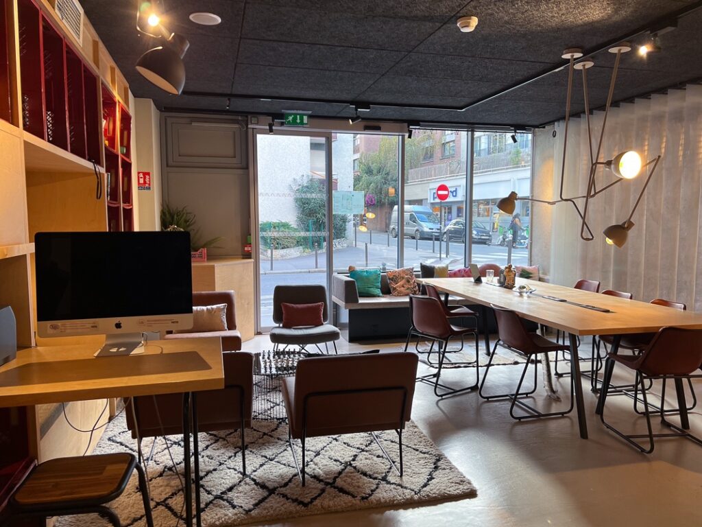Espace lounge moderne du Moxy Paris Bastille avec grande table en bois et chaises en cuir brun.