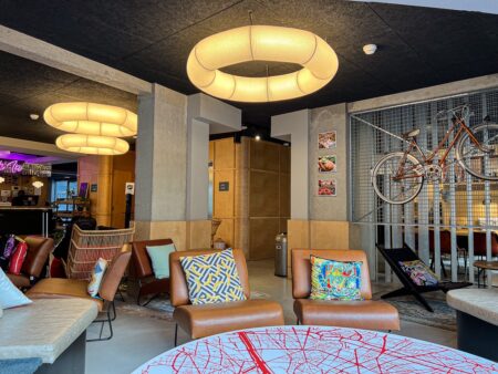 Salon design du Moxy Paris Bastille avec fauteuils colorés, grandes lampes rondes et vélo mural décoratif.