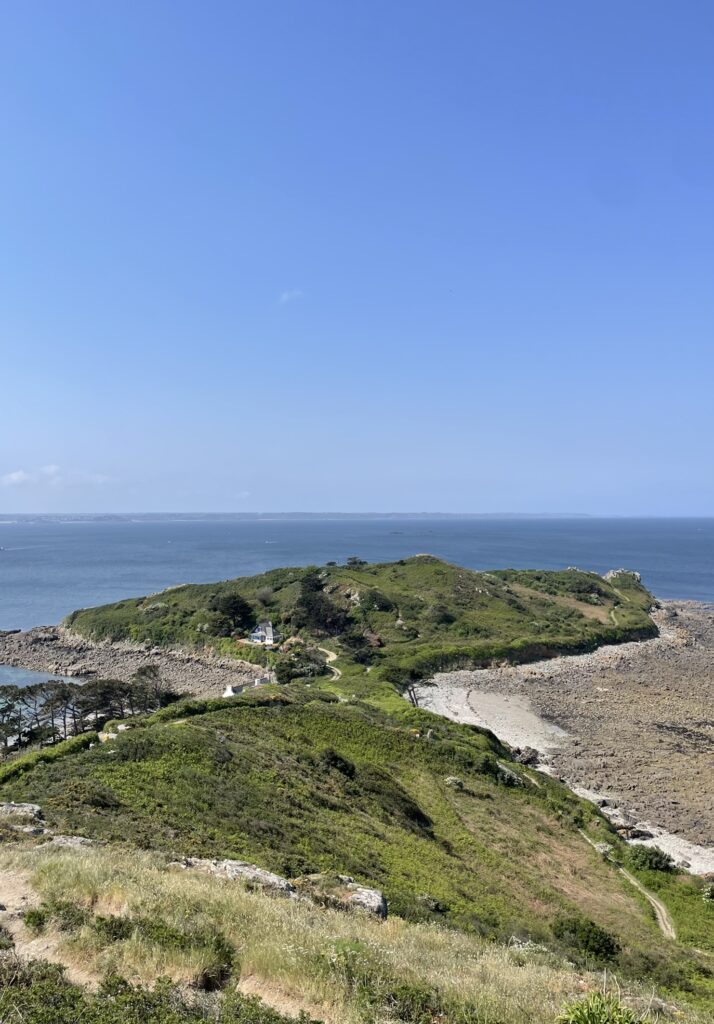 Vue aérienne d'une presqu'île verdoyante bordée de rochers et d'eau turquoise sous un ciel clair.