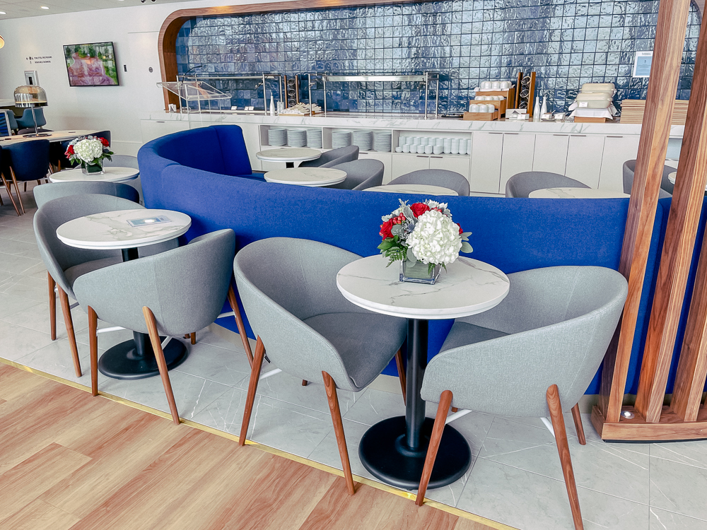 Espace moderne du salon Air France à Montréal avec tables, fauteuils gris et banquette bleue.