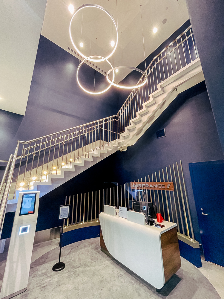Accueil moderne du salon Air France à Montréal avec escalier design et éclairage circulaire suspendu.