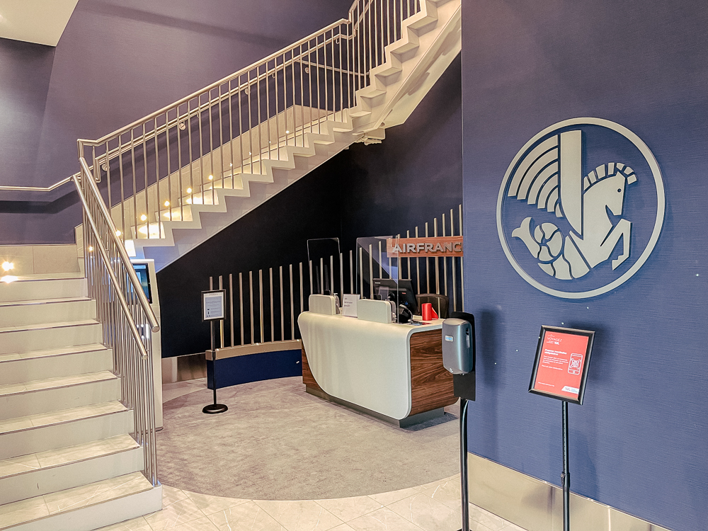 Comptoir d'accueil du salon Air France à l'aéroport de Montréal avec escalier et logo mural.