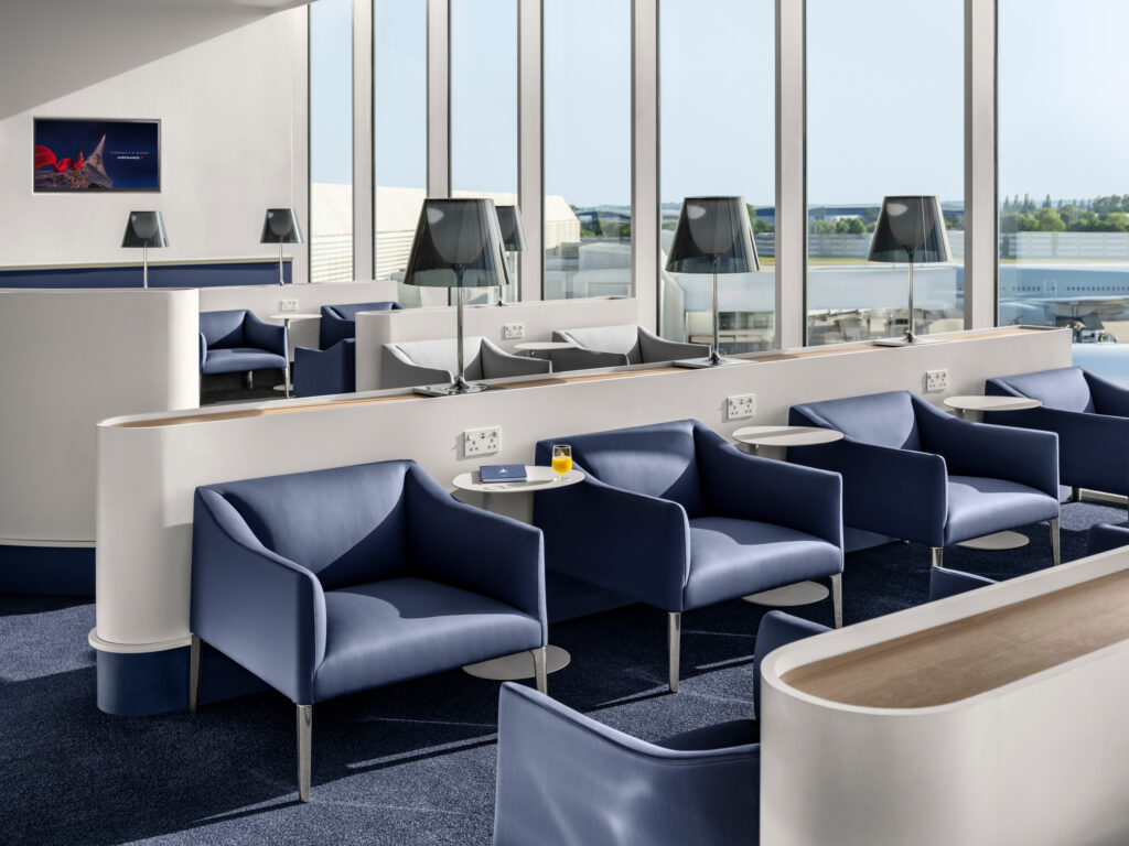 Salon Air France à Heathrow avec fauteuils bleus, lampes noires et vue sur le tarmac ensoleillé