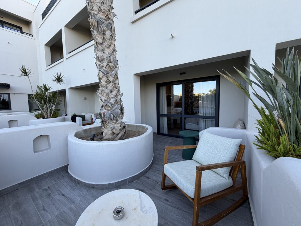 Terrasse privée du Numo Ierapetra avec fauteuil en bois, palmier et accès direct à la chambre.