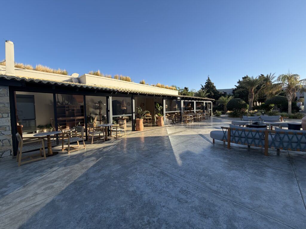 Terrasse ensoleillée du Numo Ierapetra avec tables en bois, plantes et canapés face au jardin.