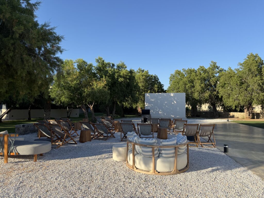 Espace extérieur avec fauteuils en bois et écran blanc sous des arbres au Numo Ierapetra.