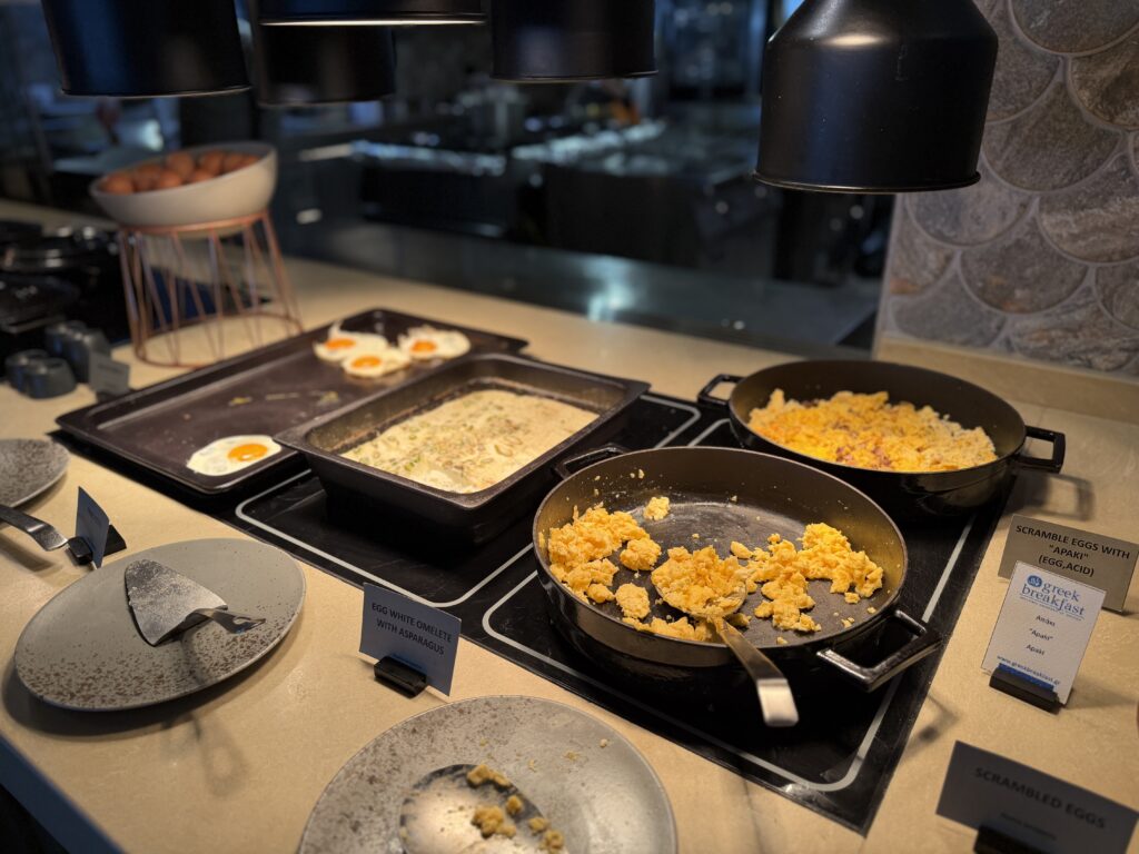 Buffet du petit-déjeuner avec œufs brouillés, œufs au plat et omelette aux asperges sous lampes chauffantes.
